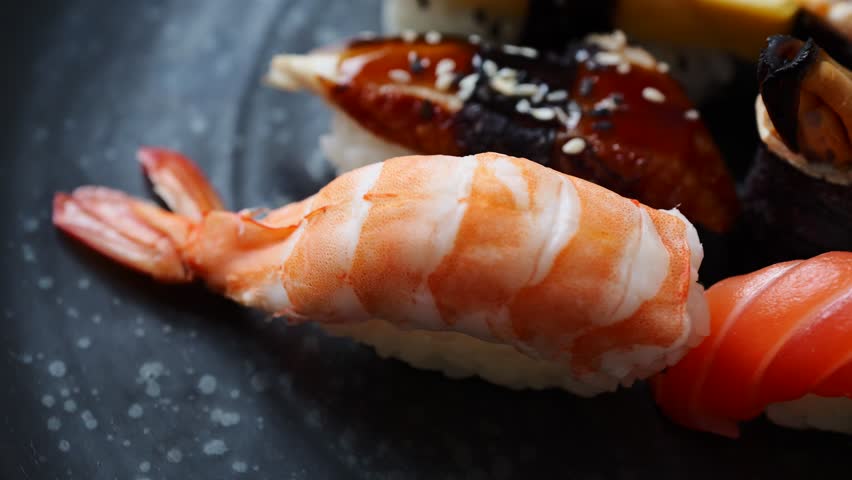 Varied presentation of gourmet Japanese sushi rolls and nigiri pieces with seafood and egg on a dark speckled plate