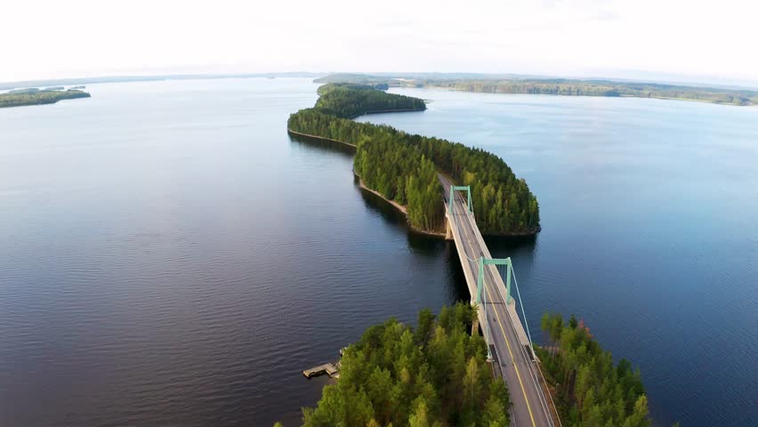 Aerial drone view of the Lakeland region in Finland, featuring a scenic bridge road connecting lush green islands surrounded by calm waterways. The vibrant landscape highlights Finland’s natural beauty, tranquil environment, and picturesque lakeside scenery in high-resolution cinematic footage.