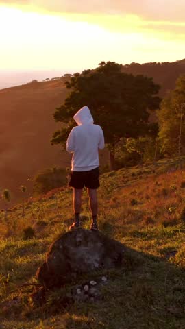 Man standing on a rock looking at a beautiful mountain landscape during a warm and golden sunset