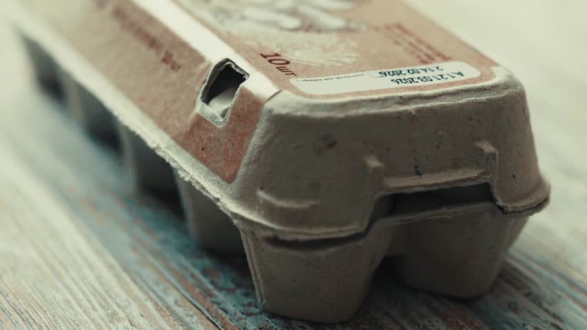  Close up of hand putting fresh eggs into a cardboard box.