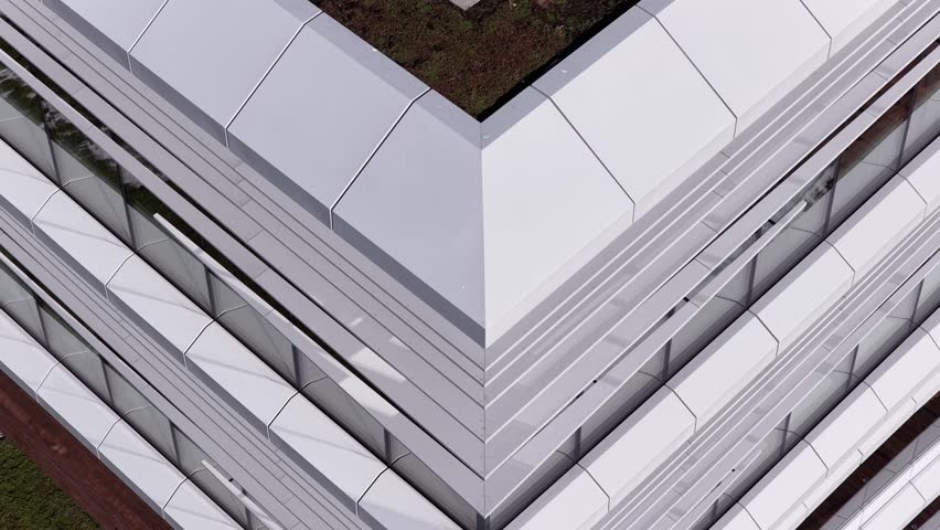 Aerial drone view of a modern office building with angular architecture, rooftop terrace, wooden deck flooring, and green roof elements in Vilnius, Lithuania.