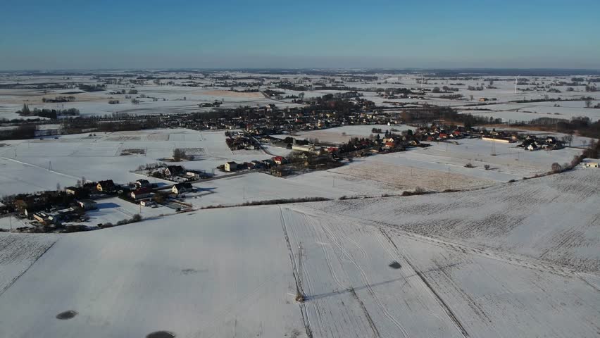 Aerial drone view of a small rural town surrounded by snow covered fields and farmland during winter. Scenic countryside landscape with houses, roads and agricultural land under snow.