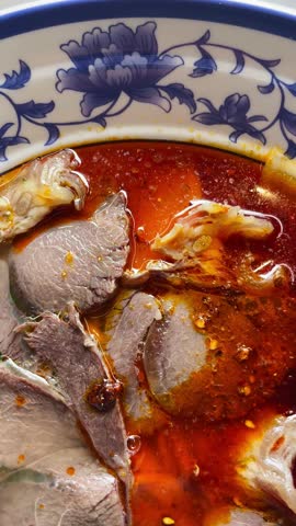 Sliced beef spicy chili oil soup closeup, blue porcelain bowl with red chili oil sheen, tender meat slices over steaming broth