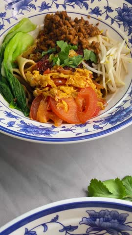 Fresh chinese noodle bowls with steaming broth, bokchoy, tomato and bean sprouts, sesame oil drizzle and scallion garnish chef