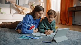 Mom help school homework talking smart schoolboy browsing tablet online lesson lying floor. Caring young woman supporting remote education reading task together. Diligent boy pupil learning subject. - Powered by Shutterstock - Get 15% off with code: PIKWIZARD15