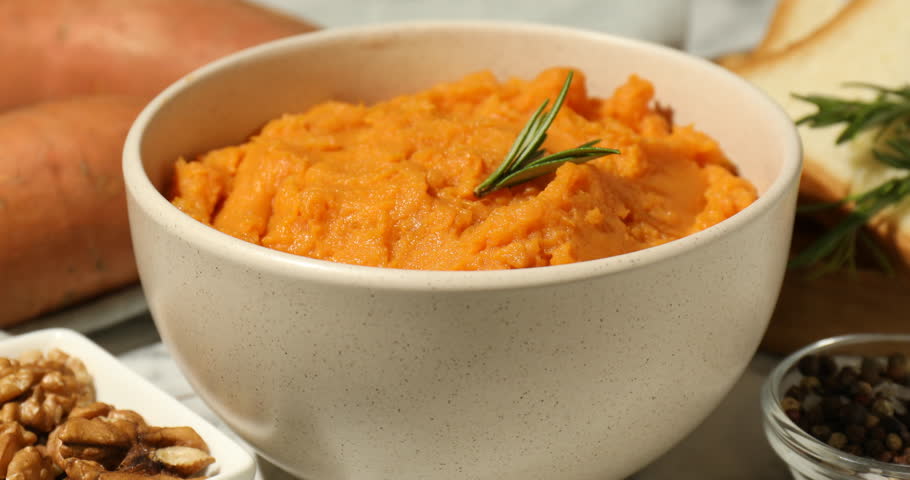 Eating tasty mashed sweet potato with rosemary at table, closeup