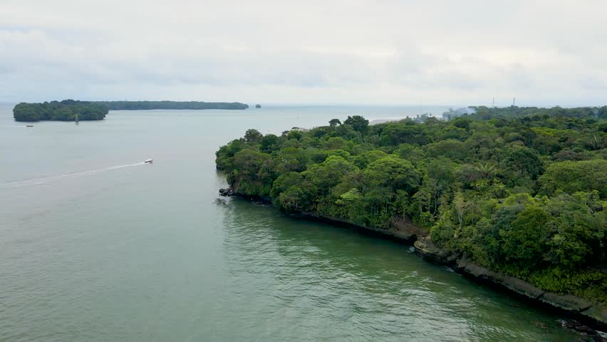 Aerial perspective showing dense green forest along the coastline, with boats on the water and a cloudy sky in Buenaventura, Colombia.