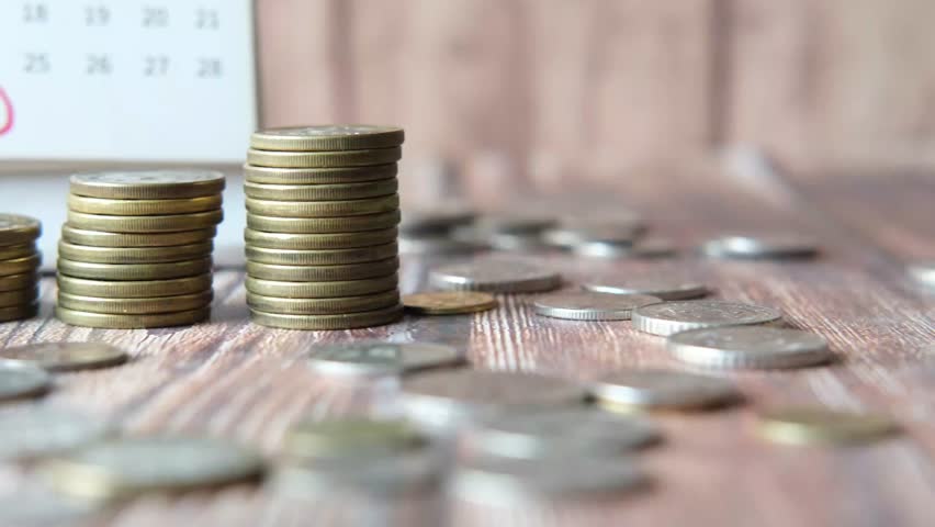 Stacking coins on wooden table with calendar and calculator showing financial growth and savings concept