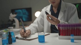 Female scientist wearing a lab coat holding a dropper bottle and writing on a clipboard in a lab - Powered by Shutterstock - Get 15% off with code: PIKWIZARD15