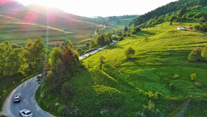 A road passes hills covered with spruce forests and meadows against a cloudy sky
