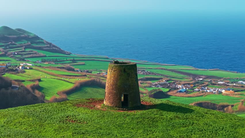 Aerial view of an abandoned stone windmill ruin standing in a green field on Sao Miguel Island, Azores, Portugal. A historic landmark overlooking the Atlantic Ocean.