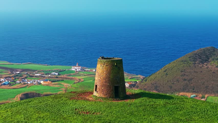 Aerial view of an abandoned stone windmill ruin standing in a green field on Sao Miguel Island, Azores, Portugal. A historic landmark overlooking the Atlantic Ocean.