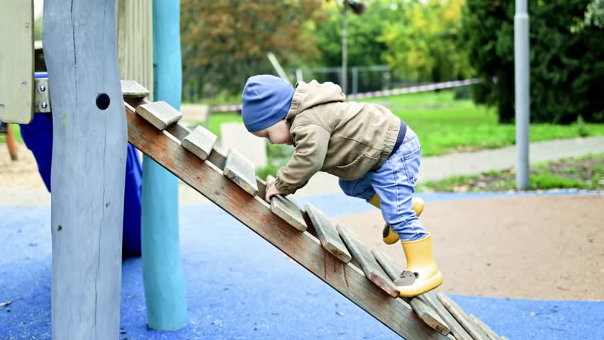 Little boy 2 years old running and playing on the playground in autumn. Toddler on a walk outdoors in the park on the playground.