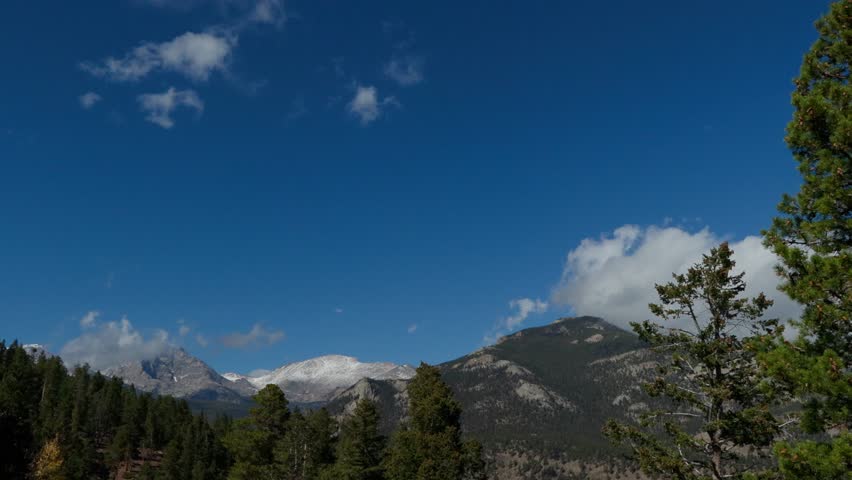 Clouds moving over the Rocky Mountains.  Static timelapse shot of white clouds rushing past the snowcapped Rocky Mountains with a clear blue sky in the background in late fall. 