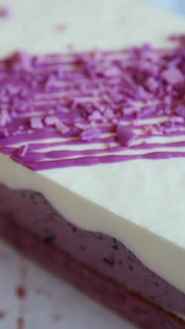 Delicious slice removed from a purple cake with white topping and berry mousse, served on a plate over a checkered tablecloth.