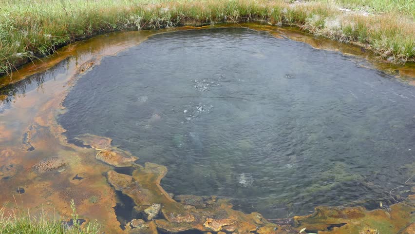 Small geothermal hot spring bubbling and steaming in Yellowstone National Park with mineral deposits and colorful bacterial mats surrounding the water pool, Nature geology, Travel tourism