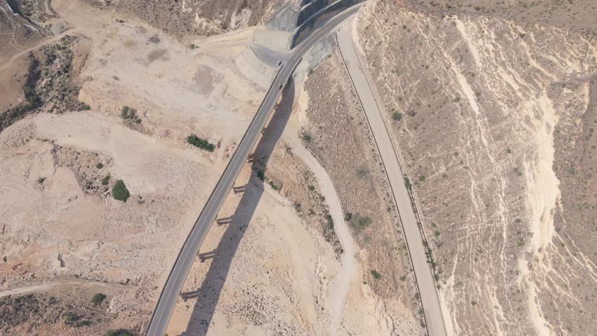 Aerial view of a concrete bridge and winding mountain roads with moving vehicles in an arid desert landscape in Iran.