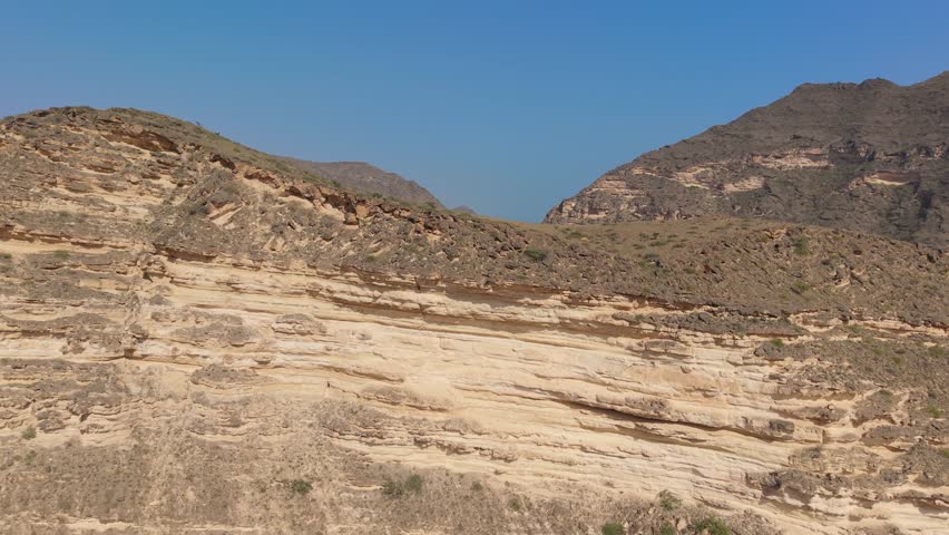 Aerial view of stratified rock formations and a winding road through an arid mountain valley near the coast in Iran.
