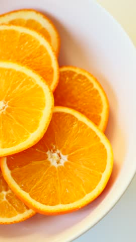Vibrant orange fruit slices are stacked neatly on a clean white bowl. They appear fresh and juicy, ready to be enjoyed.
