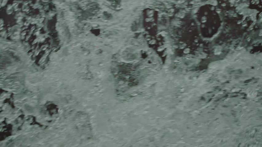 Close up of whitewater foam and spray moving across the frame, with bubbles and turbulent water texture.