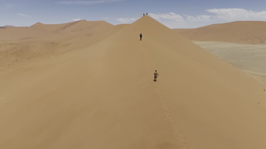 Drone flies low over the backs of hikers as the summit Dune 45 on windy and on sunny day in Sossusvlei, Namibia