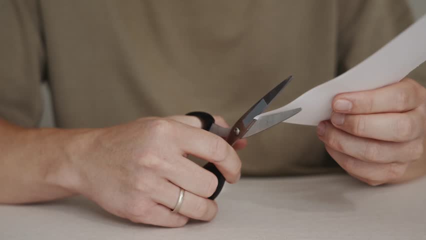 Close-up of hands cutting a sheet of paper with scissors. Simple manual action showing paper cutting process on a table.High quality 4k footage