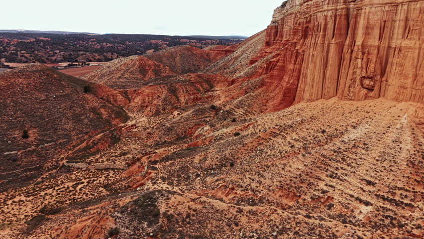 A canyon stretches across the landscape with steep rocky sides and dry ground. Small plants dot the scene under a cloudy sky. The view highlights the unique shapes of the formations.