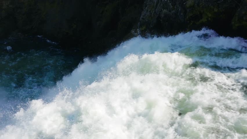 Foaming river rapids surge and crash through a rocky canyon channel, powerful whitewater turbulence, closeup waterfall water, slow motion