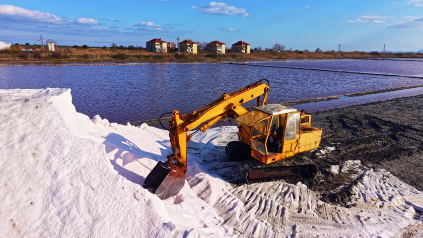 A bright yellow excavator moves through the shimmering salt, sculpting the landscape by the water