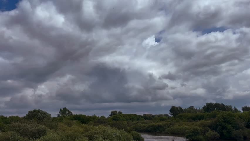 Gray clouds in the sky over the river between the trees.