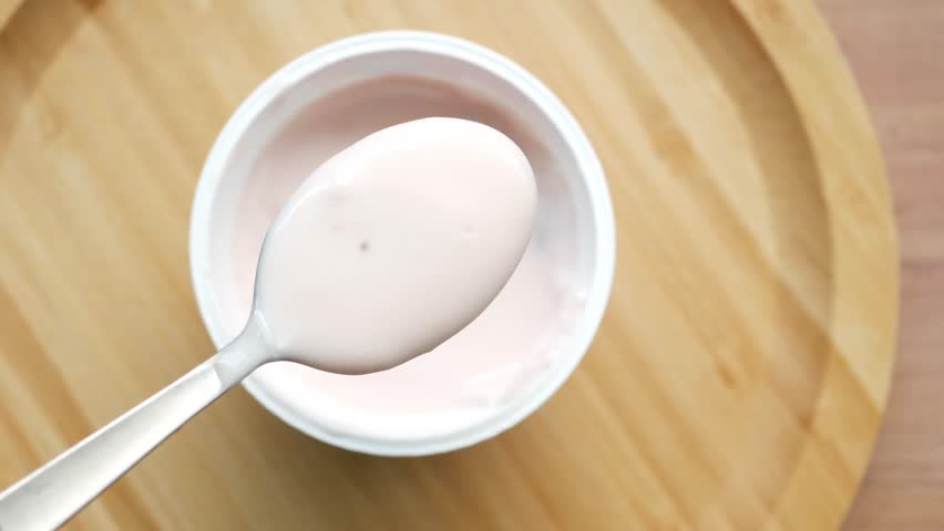 Fresh strawberry yogurt on silver spoon above white cup with wooden plate background