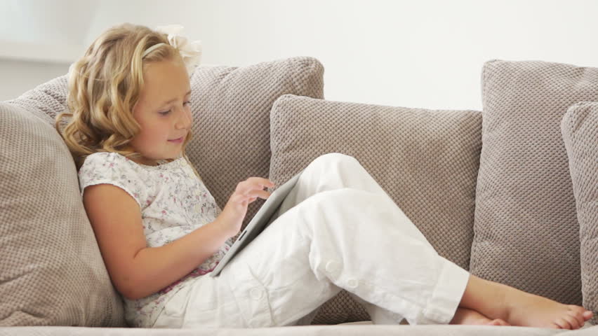 Girl sitting on couch with tablet pc and smiling
