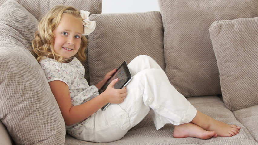 Little girl lying on couch and playing on tablet pc
