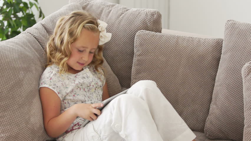 Girl sitting on couch and playing on tablet pc
