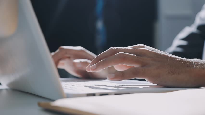 Accountant reviewing printed financial reports at messy office desk with calculator and sticky notes under soft window daylight for audit and corporate finance work