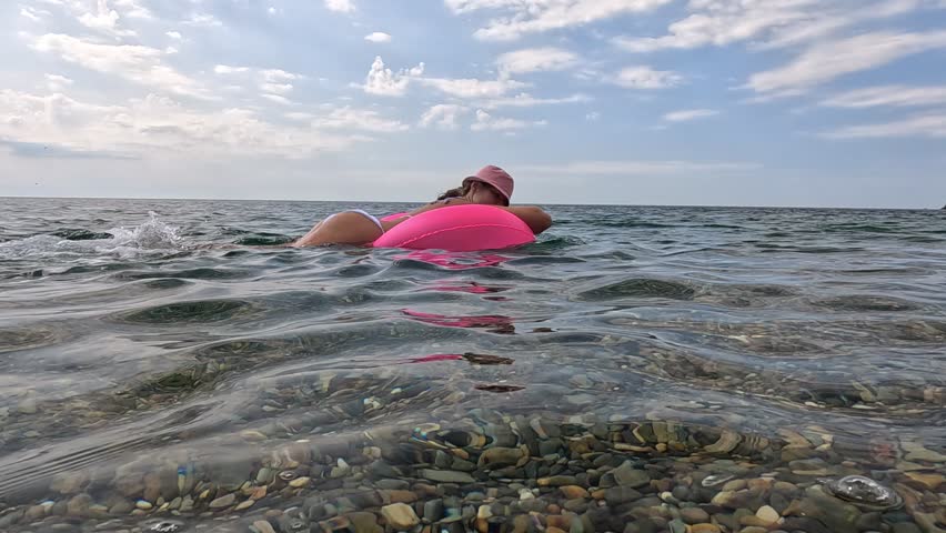 Woman Beach Floating - A woman in a pink swimsuit floats in the water at a beach on a sunny day.