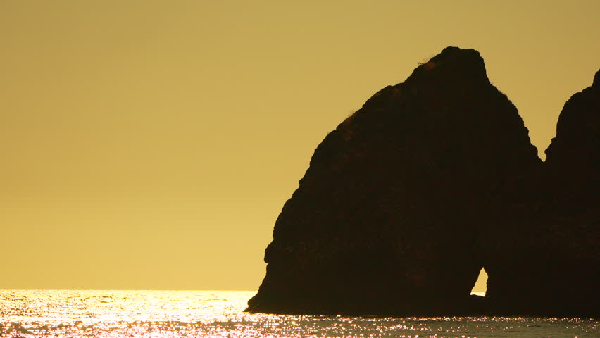 Sea rock sunset beautiful golden sky over sparkling water with silhouetted rock formation at dawn