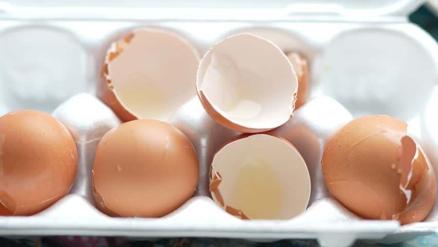 Six brown eggs with cracked shells in white carton, revealing shiny yolks and whites.