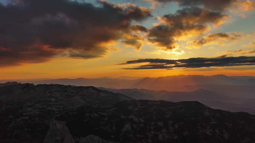Orange sun setting over mountain with dramatic clouds. Evening sky at sunset with orange light, aerial view, panorama 4k