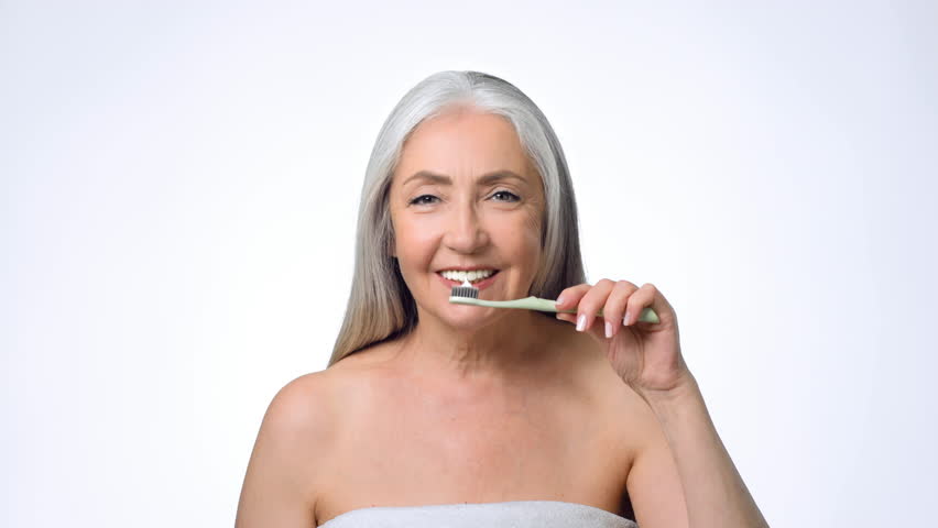 Senior Woman With Gray Hair Brushes Her Teeth in a Bright Bathroom Setting