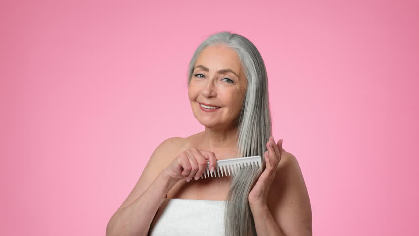 Woman With Long Gray Hair Smiles and Gestures in Front of a Pink Background