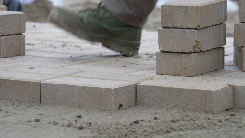 Laying paving slabs close-up. Sidewalk repair. Worker laying stone paving slab. Laying tiles in the city park garden. Laying gray concrete paving slabs in house courtyard on sand foundation base.
