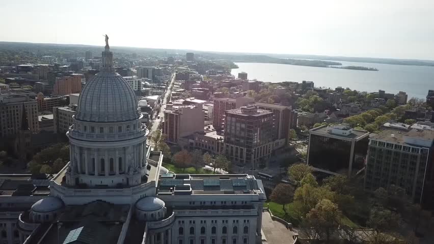 Drone aerial view of a historic capitol building with large dome surrounded by city streets and government district.