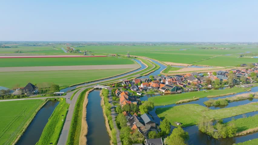 Stunning horizontal aerial overview of a rural Dutch village. Featuring traditional houses, narrow canals, and symmetrical agricultural fields. Authentic Holland landscape.
