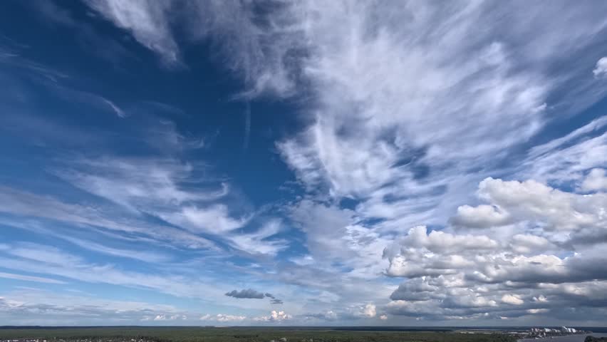 Fast moving white clouds drift across a wide blue sky above a vast green landscape. Experience the day