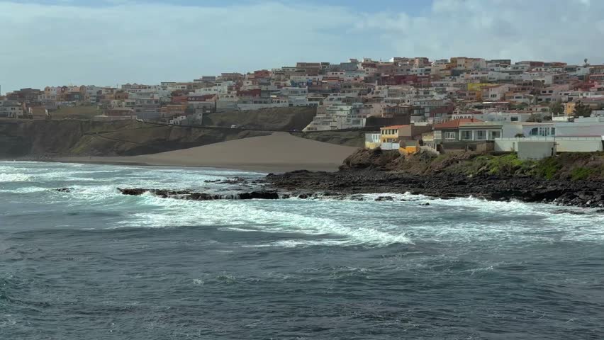 Ocean Waves Crashing on a Rocky Shoreline with a Scenic Coastal Town on the Hillside
