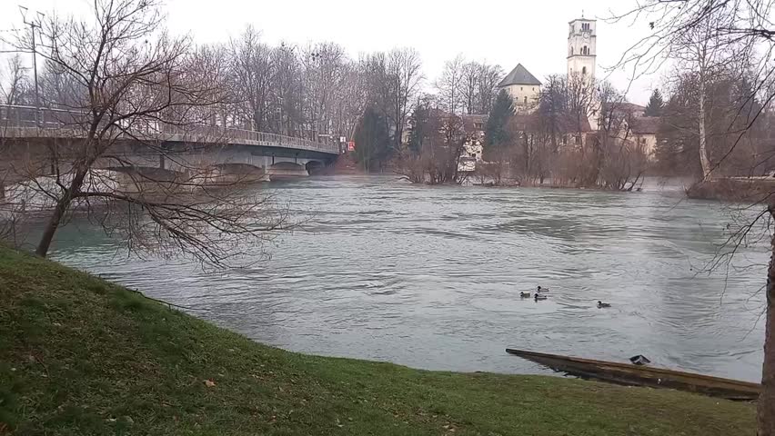 River Flowing Through Town with Bridge and Ducks on Water
