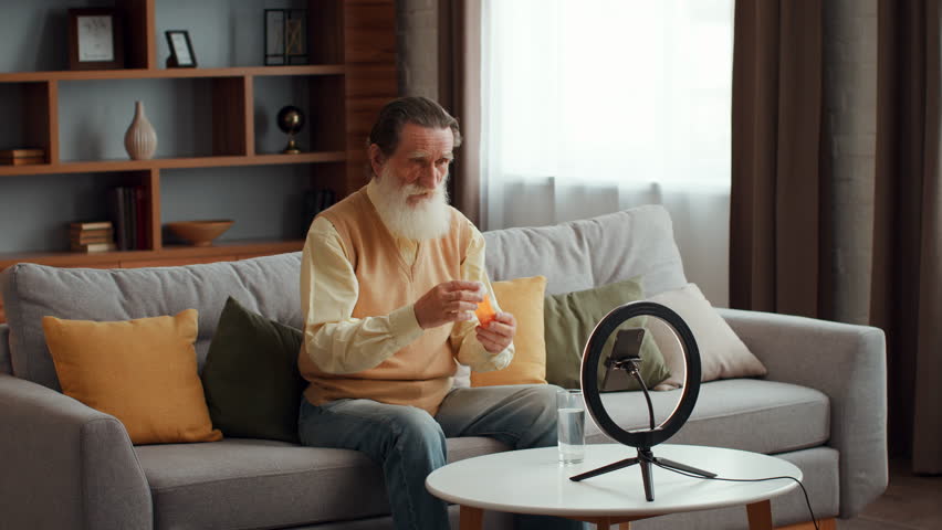 Senior man recording video instruction about first medical aid if having heart attack, showing pills to smartphone