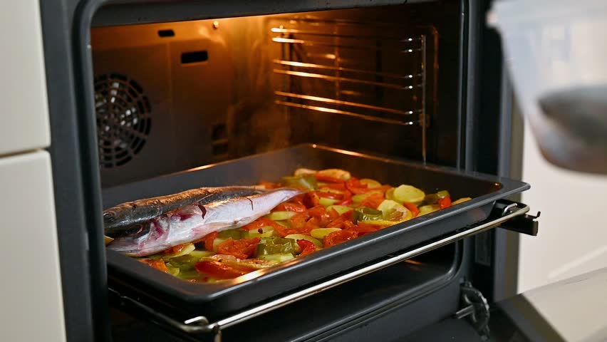 Horizontal video of a hand placing fresh horse mackerel fish on top of a tray with roasted potatoes, peppers, tomato and lemon before returning it to the oven. Seafood preparation for a healthy Mediterranean baked fish recipe, concept of nutritious ingredients, omega-3 rich diet and home seafood cooking