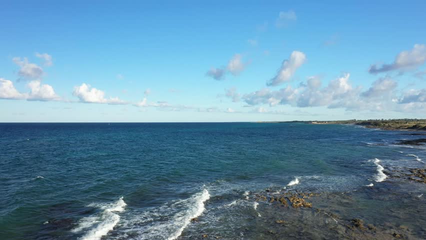 Aerial view of the clear blue sea and rugged coastline near Brindisi, Italy, under a bright sky with scattered clouds. Tranquil Mediterranean scenery ideal for travel and nature concepts.